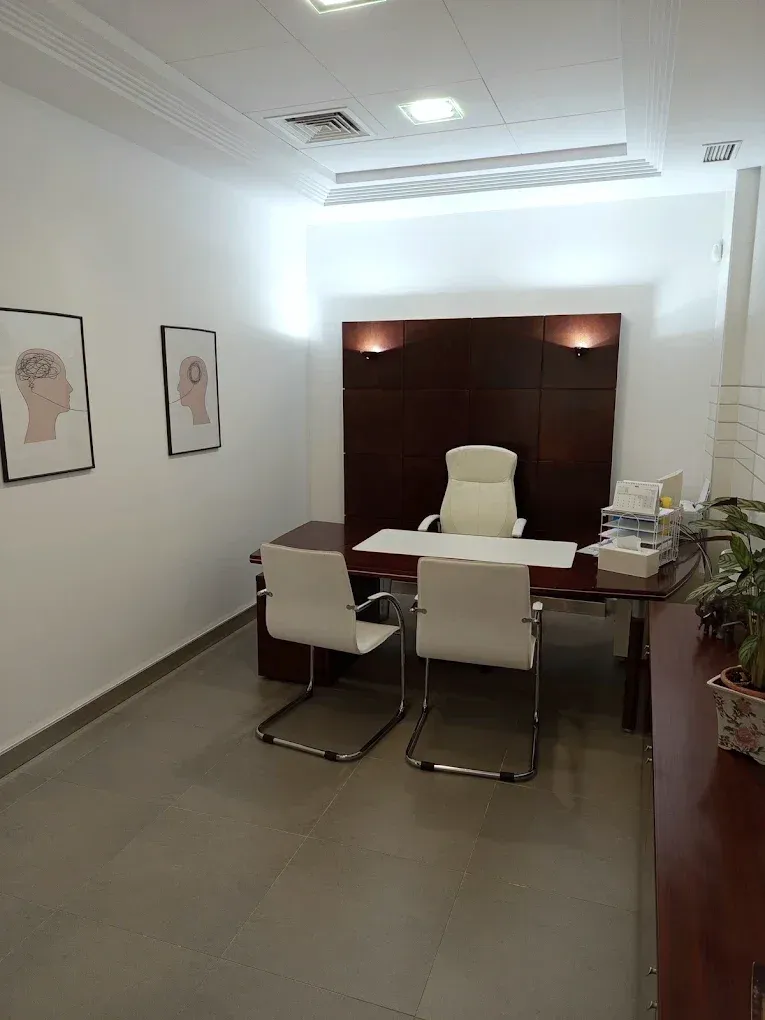 Despacho de consulta con mesa de madera oscura y dos butacas.